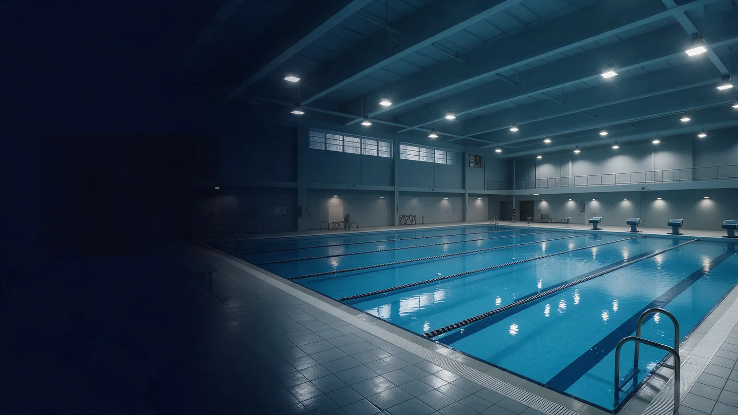 Visualisation d’une piscine couverte éclairée, avec ses lignes de nage et les reflets sur l’eau.